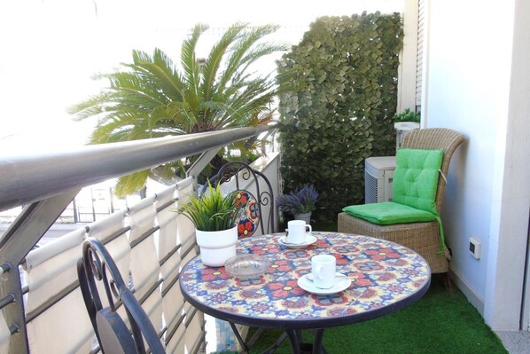 A small outdoor balcony with a round table, two chairs, a potted plant, and a decorative wall.