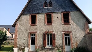Ein zweistöckiges Haus mit steiler Mansardedecke, einer Steinaußenwand und zahlreichen Fenstern mit Fensterläden.