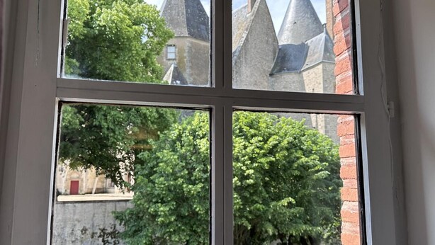 Ein Fenster mit vier Fenstern, jedes bietet Blick auf ein Gebäude mit spitzer Dachform und Ziegelwänden.