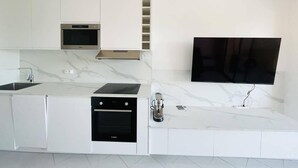 Eine moderne Küche mit weißen Schränken, einem eingebauten Ofen, einer Mikrowelle und einem an der Wand befestigten Flachbildfernseher.