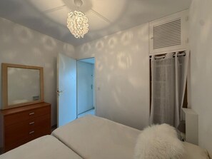 A bedroom with a bed, a dresser, a mirror, a door, and a ceiling light fixture. - Calvi: 2 Room Apt 4 Pers, AC, Terrace, Parking, Near Beach (Calvi)