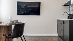 A modern kitchen with a flat-screen TV mounted on the wall, a dining table with chairs, and a built-in sink. - Swan Deluxe Studio for 4 guests (Reykjavík)