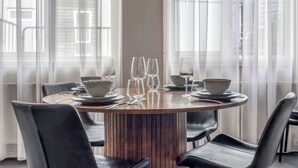 A round dining table with chairs, set for a meal, in a room with large windows and sheer curtains. - Swan Deluxe Studio for 4 guests (Reykjavík)