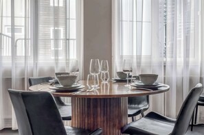 A round dining table with chairs, set for a meal, in a room with large windows and sheer curtains. - Swan Deluxe Studio for 4 guests (Reykjavík)