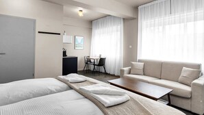 A modern hotel room with two beds, a sofa, a small table, a desk, and a dining area. - Swan Deluxe Studio for 4 guests (Reykjavík)