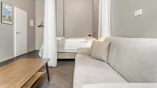 A modern bedroom with a bed, a sofa, a wooden table, and a hanging light fixture. - Swan Deluxe Studio for 4 guests (Reykjavík)
