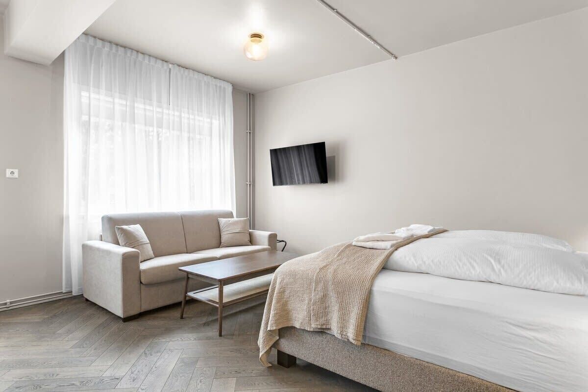 A modern, minimalist bedroom with a sofa, a bed, and a TV mounted on the wall.