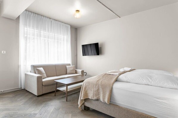 A modern, minimalist bedroom with a sofa, a bed, and a TV mounted on the wall.