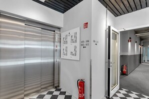 A hallway with a fire extinguisher, a fire alarm, and a door leading to another room.
