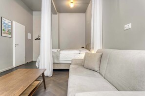 A modern bedroom with a bed, a sofa, a wooden table, and a hanging light fixture.