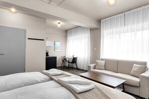 Quarto de hotel moderno com duas camas, um sofá, uma mesinha, uma escrivaninha e um espaço de refeições.