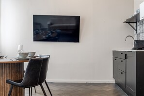 A modern kitchen with a flat-screen TV mounted on the wall, a dining table with chairs, and a built-in sink.