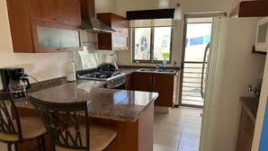 Une cuisine avec un îlot central, une cuisinière, un évier et un réfrigérateur. Il y a trois chaises autour de l’îlot.