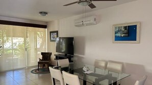 Un coin repas avec une table et des chaises en verre, un ventilateur de plafond et un téléviseur fixé au mur.
