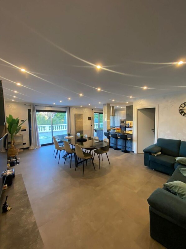 A spacious living area with a dining table and chairs, a sofa, and a kitchen area visible through an open door. - Villa Isabella: Relaxation, tranquility, a pool, and beautiful nearby beaches (Ventimiglia)