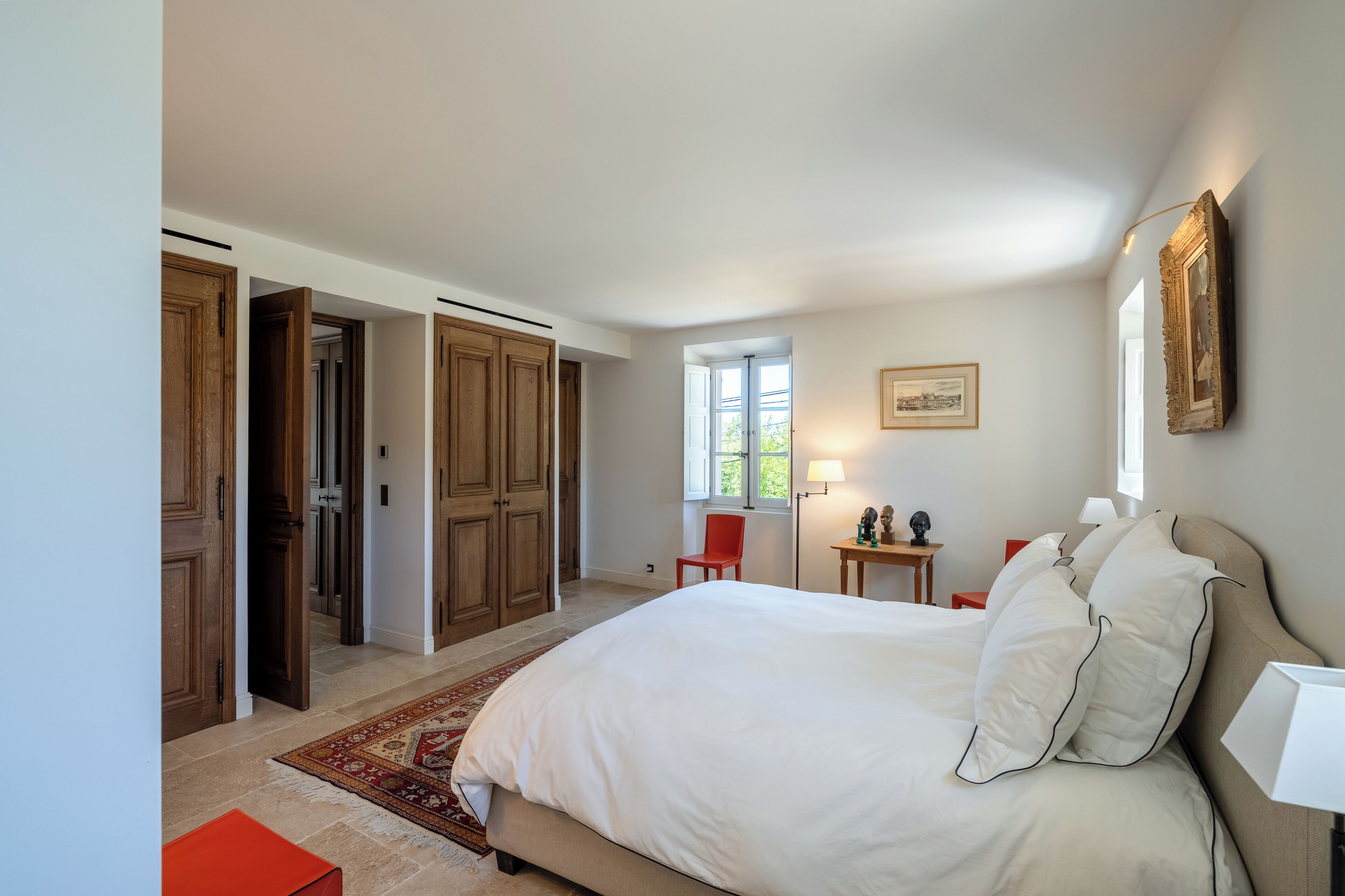 Un dormitorio con una cama grande, una silla roja, una mesita y armarios de madera.