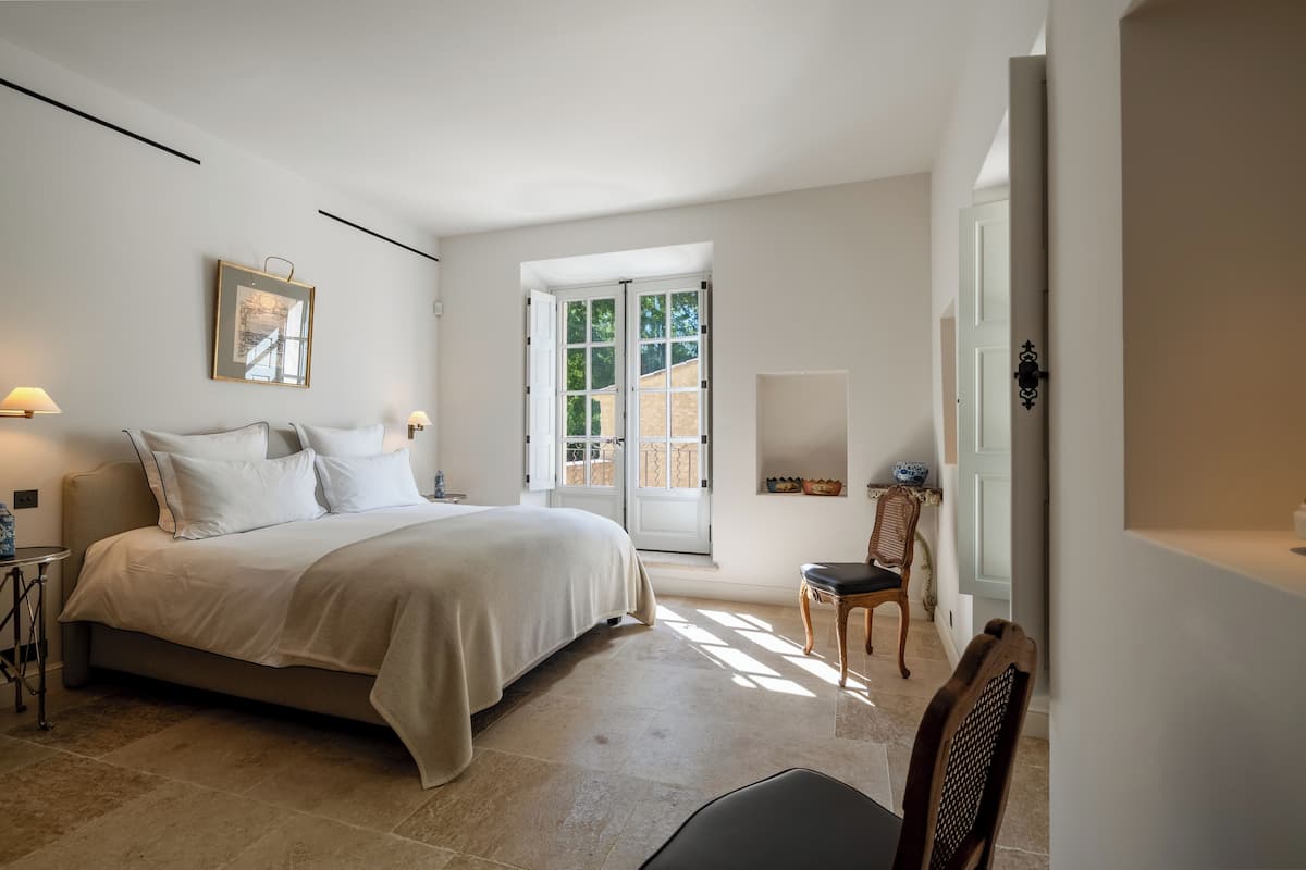 A bedroom with a bed, bedside tables, a chair, a window with a view, and a door.