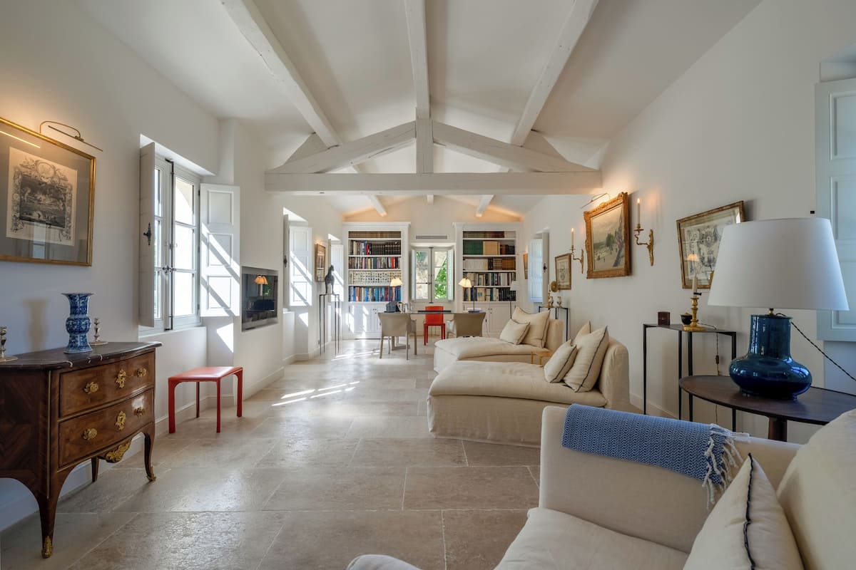 A spacious living area with a high ceiling, a fireplace, a sofa, a coffee table, and a bookshelf.