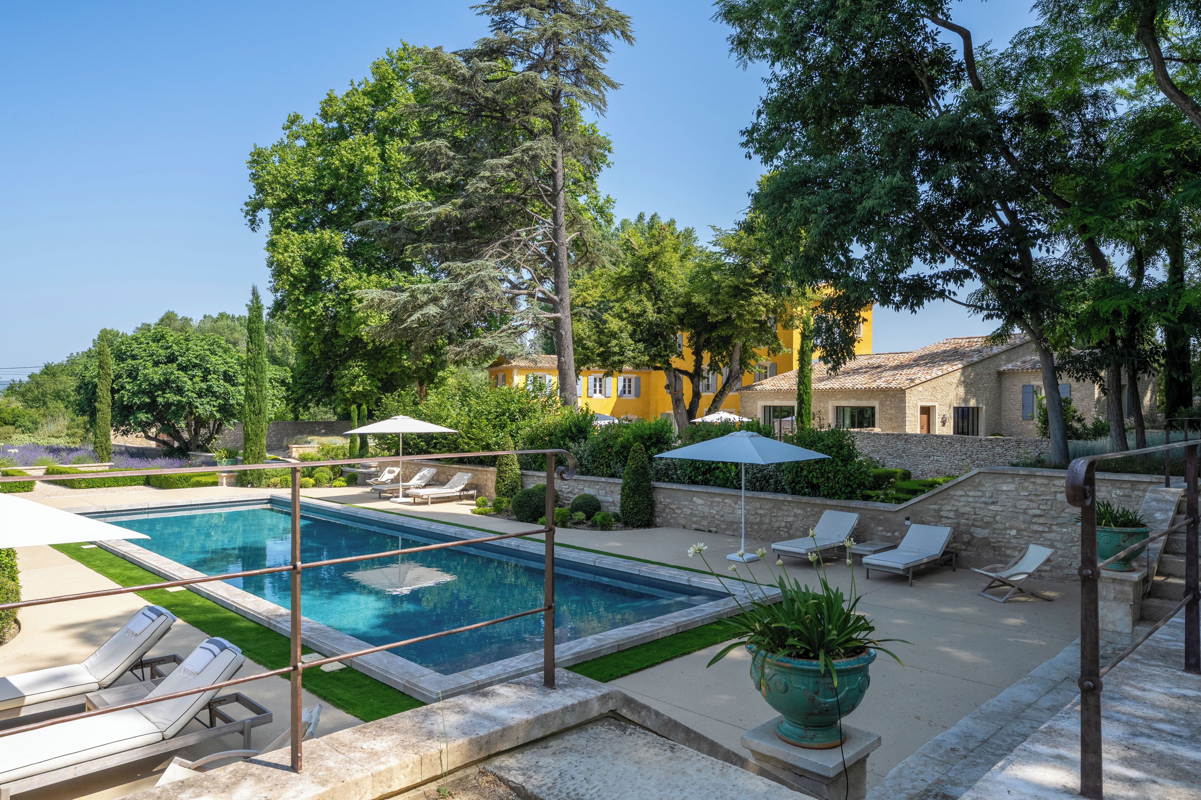 A swimming pool with sun loungers and umbrellas, surrounded by greenery and stone walls.