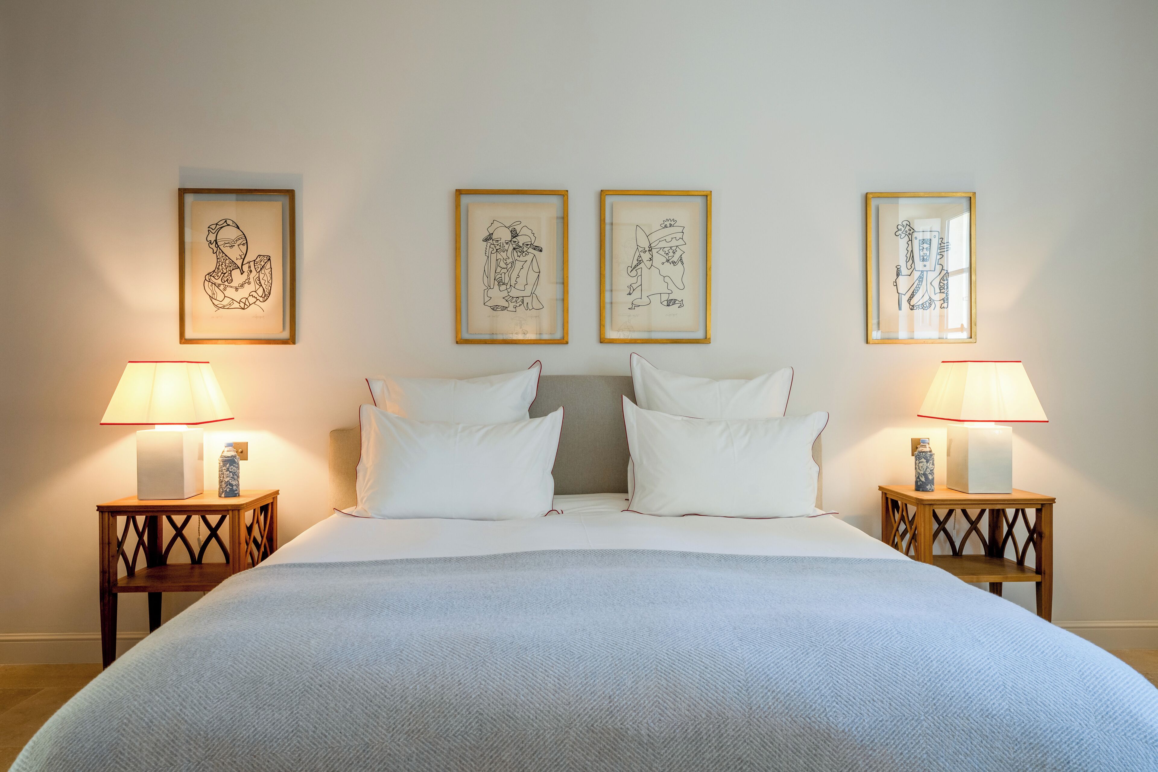 A neatly made bed with white linens, two bedside tables with lamps, and three framed artworks on the wall.