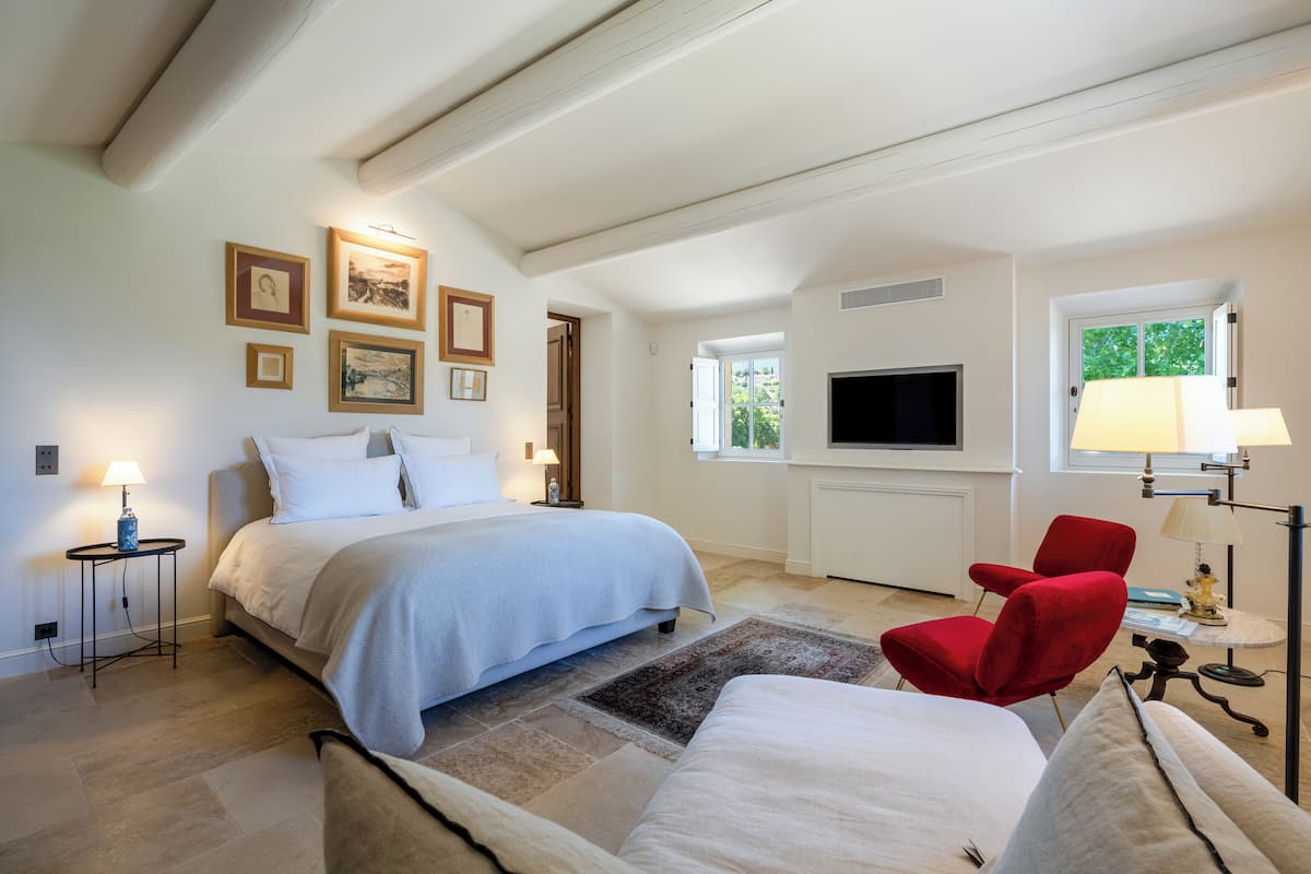 A bedroom with a bed, a TV, a red chair, and a lamp.
