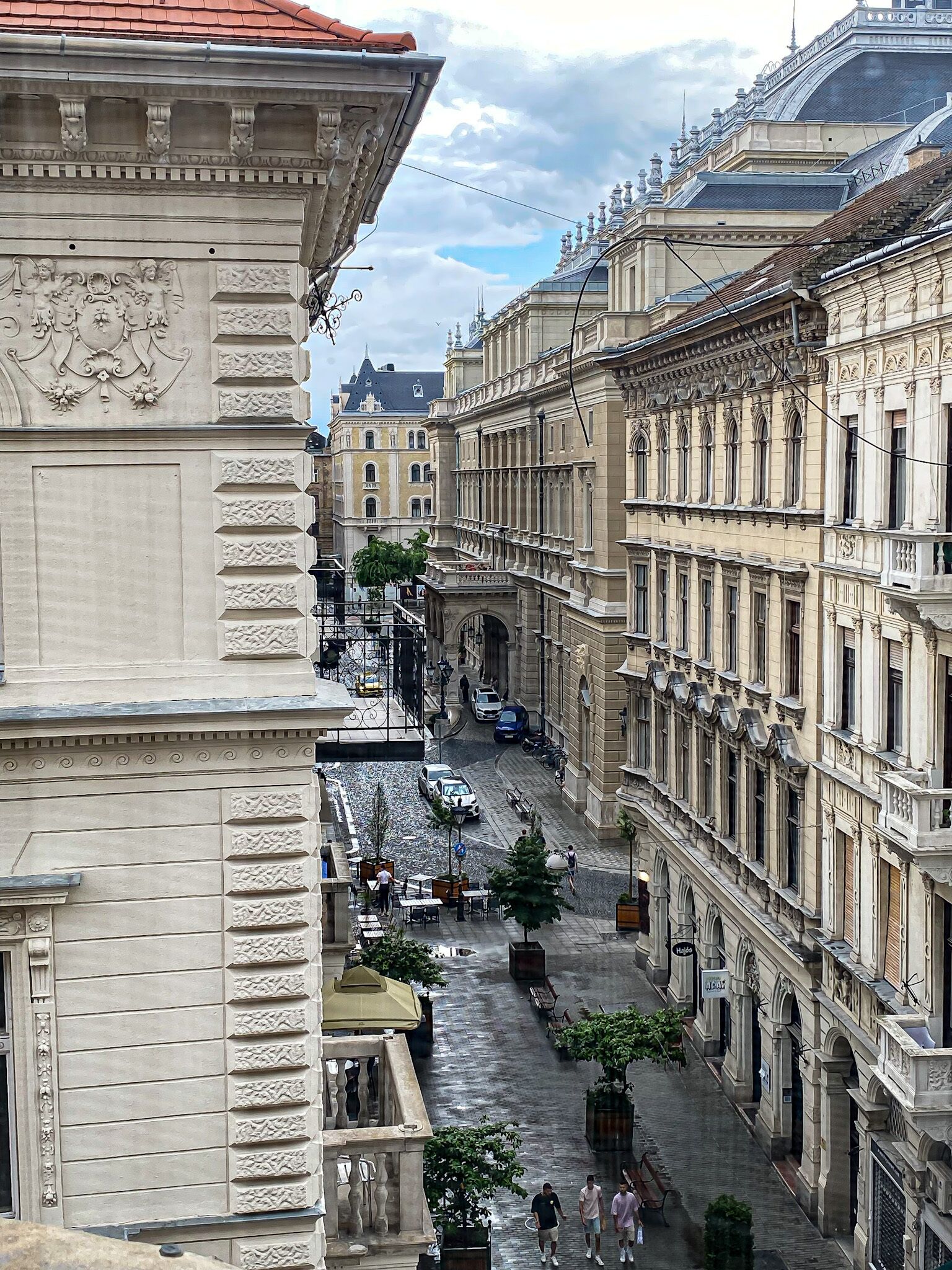 A historic street with ornate buildings, a cobblestone road, and outdoor seating areas.