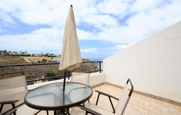 Un balcon avec une table en verre, des chaises et un parasol beige.