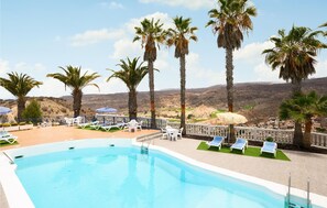 Un espace piscine agrémenté de chaises longues et de palmiers, offrant une vue sur un paysage montagneux.