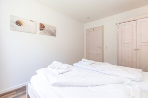 Une chambre à coucher propre et moderne, avec un lit bien fait, deux portes en bois et deux œuvres d’art accrochées au mur.