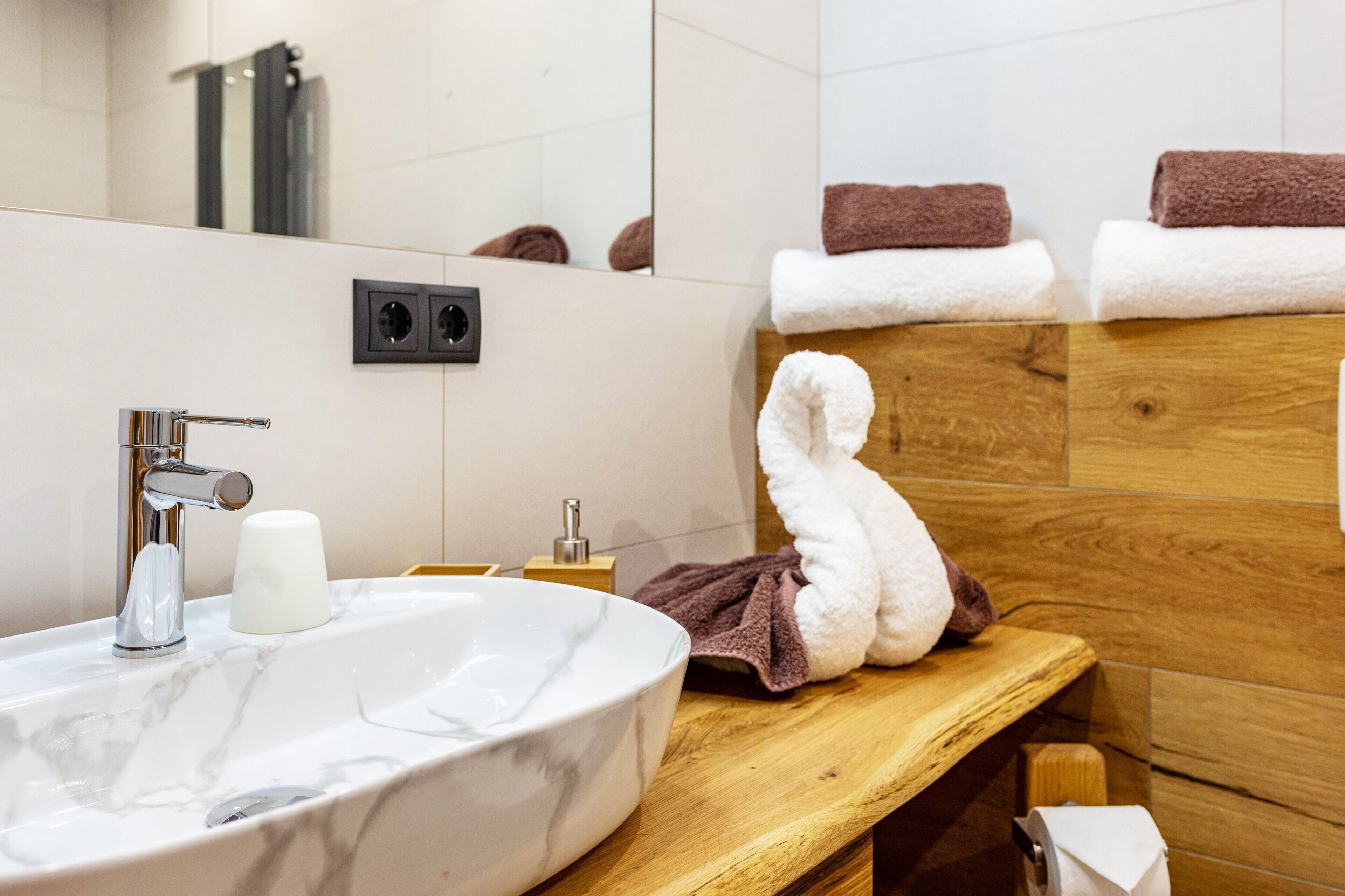 Ein Badezimmer mit Marmorwaschbecken, einem Spiegel, einem Holzwaschtisch und Handtüchern.