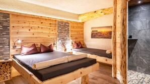 A wooden room with a bed, a bench, a stone wall, and a fireplace.