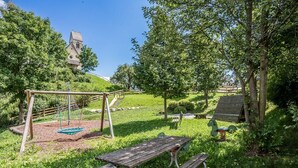 A playground with swings and a slide, surrounded by trees and a picnic table.