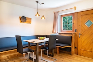 Un coin repas avec une table en bois, des chaises noires, un banc et une horloge au mur.