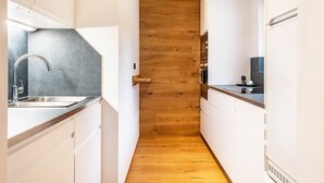 A narrow kitchen with white cabinets, a wooden floor, and a stainless steel sink.