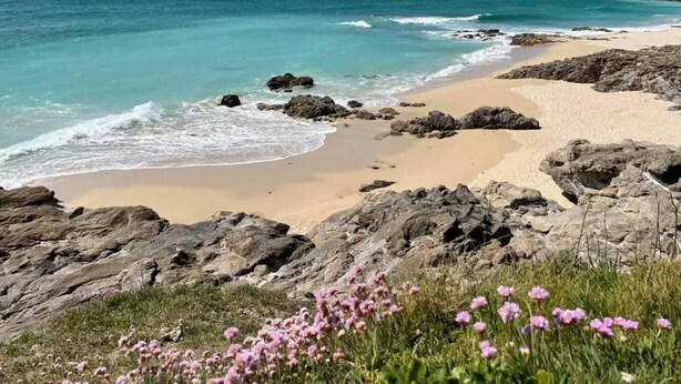 A beach with clear turquoise water, sandy shore, and rocky outcrops.