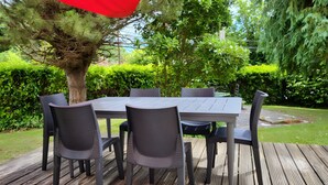 A wooden deck with a table and chairs, surrounded by greenery.