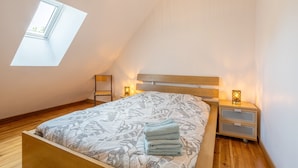 A bedroom with a sloped ceiling, a skylight, a bed with a patterned bedspread, two bedside tables with lamps, and a wooden headboard.