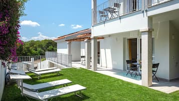 Una casa moderna de dos pisos con balcón, césped cuidado y mobiliario exterior.