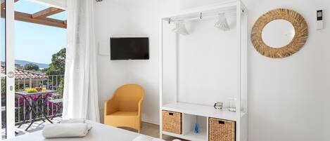A hotel room with a bed, a chair, a TV, a wardrobe, and a balcony with a table and chairs.