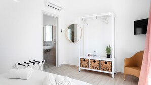 A modern hotel room with a bed, a white console table with wicker baskets, a round mirror, and a television on the wall. - Sardegna è - New rooms (Olbia)