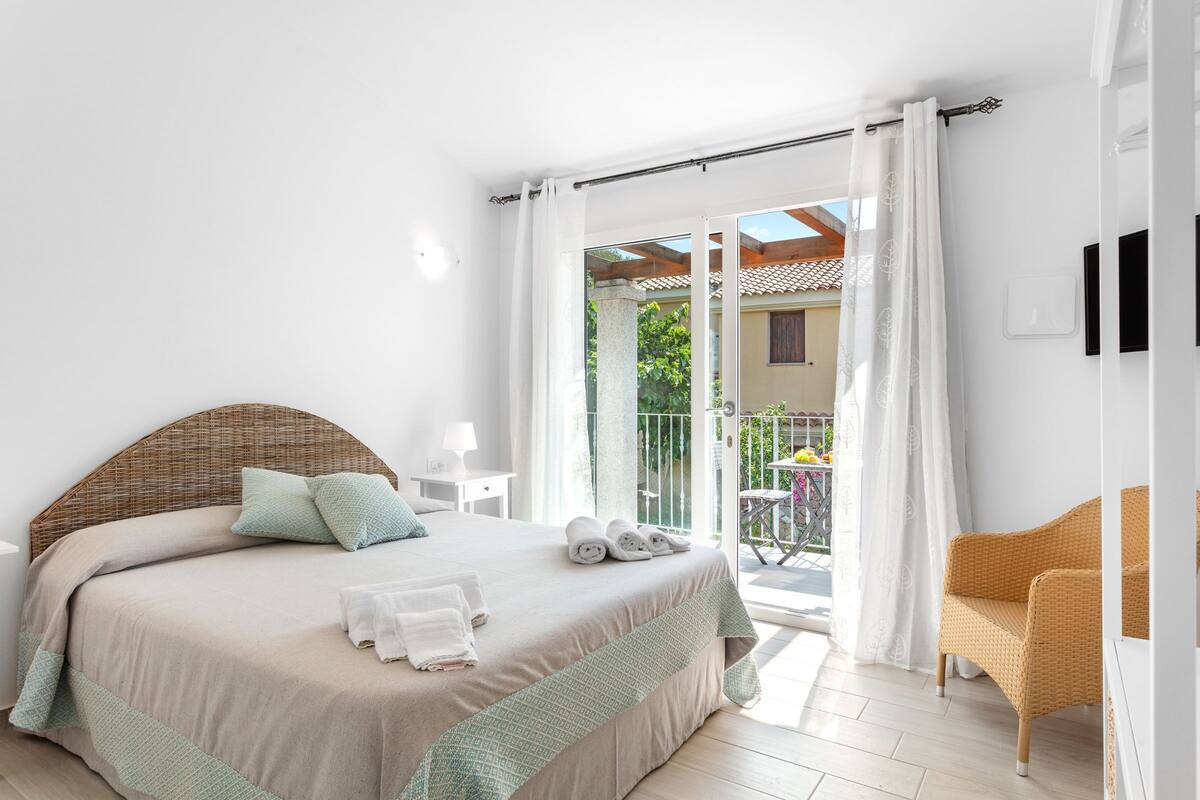A bedroom with a bed, a chair, and a balcony with a table and chairs.