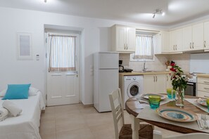 A compact kitchen with a washing machine, a dining table with plates, and a bed with a blue pillow.