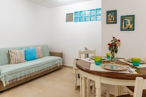 A living room with a sofa, a dining table with chairs, and a small window.