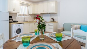 Une cuisine compacte avec des meubles blancs, un lave-linge et un coin repas agrémenté d’une table ronde pour deux personnes.