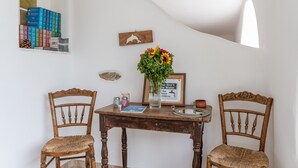 Une pièce avec un mur blanc, une table en bois, deux chaises en bois, un vase de fleurs, un tableau encadré et une pile de livres.