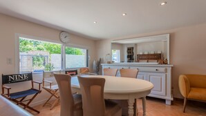 A dining area with a round table, beige chairs, a director's chair, a kitchen counter with a mirror, and a clock on the wall.