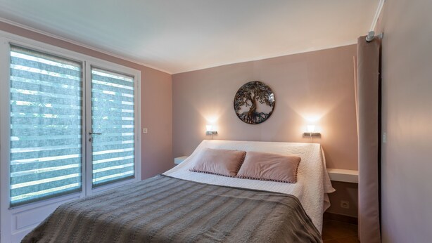 A bedroom with a bed, two bedside lamps, a wall art piece, and a window with blinds.