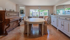 A dining area with a round table, chairs, a wooden cabinet, and a window with a view of the outside.