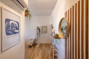 Un couloir avec un plancher en bois, une œuvre d’art encadrée, une étagère avec des plantes et un miroir au mur.