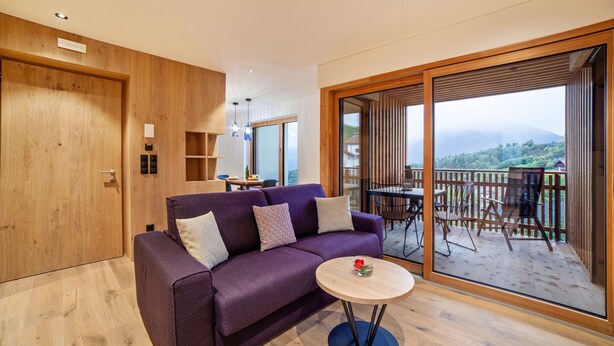 Ein modernes Wohnzimmer mit einem violetten Sofa, einem kleinen runden Tisch und einem Balkon mit Gartenmöbeln.